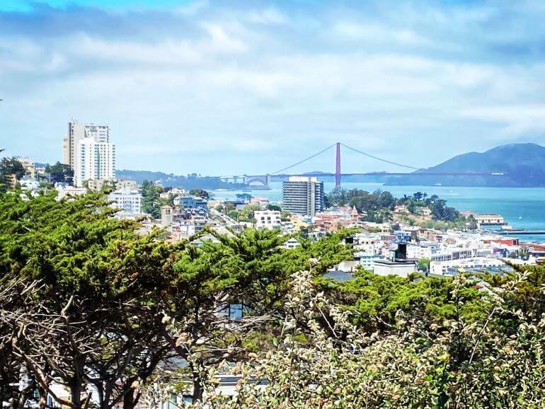View of Golden Gate Bridge beyond the rooftops of San Francisco seen from the base of Coit Tower